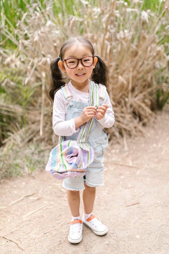 Happy child with eyeglasses, wearing denim overalls, smiling outdoors in nature.